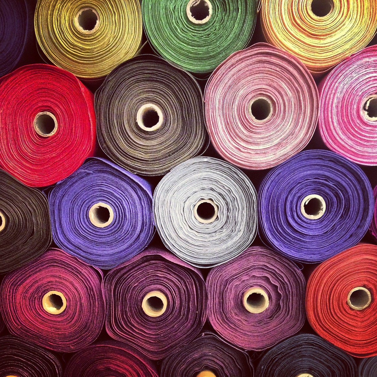 Colorful array of fabric rolls arranged in rows, showing various shades including red, purple, pink, green, and yellow